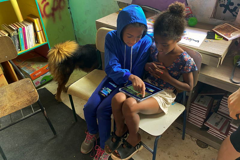 A young person helps a friend learn how to code OctoStudio projects in Brazil.