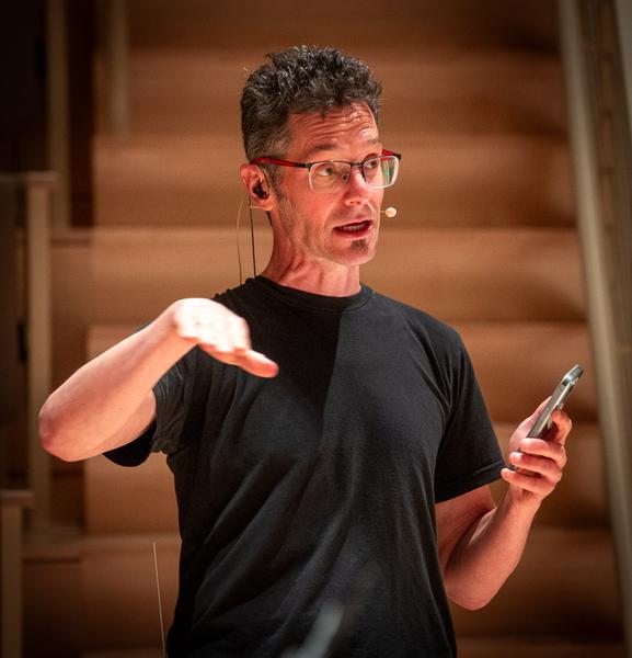 Caption:MIT professor of the practice Eran Egozy explains cellphone usage to an audience for the performance of his piece, “EV6.”